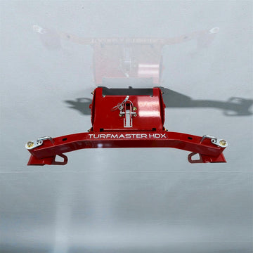 A red metal Toro 30" TurfMaster HDX Caster Swivel Wheel Kit is attached to a gray surface and viewed from above. Bolts and a pin secure the kit, which casts a faint shadow.