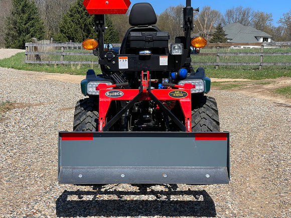 Rear view of a compact red tractor with a gray front blade and signaling lights, ideal for landscaping tasks.